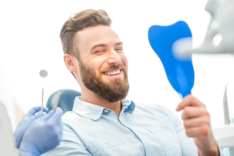 Man in a dental chair looking at his smile in a mirror