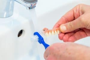 Person holding dentures and brushing them with toothbrush and water