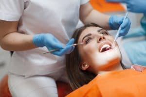 Woman laying down in dental chair while hygienist works on her teeth.