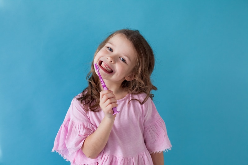 Little girl smiling with a toothbrush in her mouth.