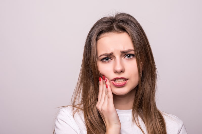 Woman holding hand against jaw in pain