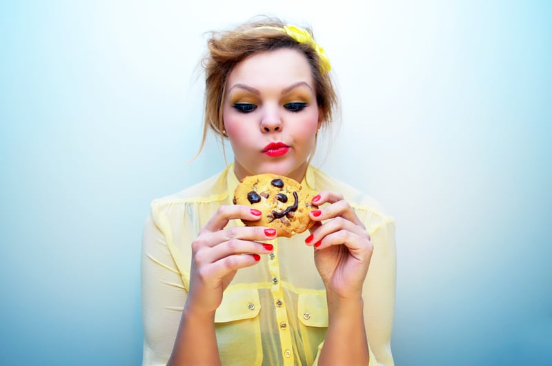 Young woman about to eat a chocolate chip cookie, but she is deciding to actually eat it or not. 