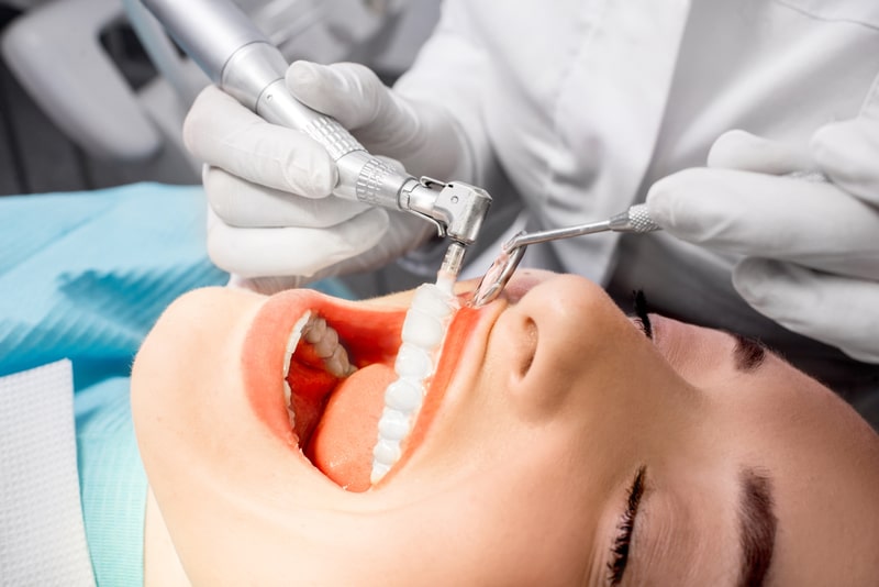 View of a woman having a dental cleaning done by a dentist.