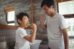Asian father and son brushing their teeth together in the bathroom.