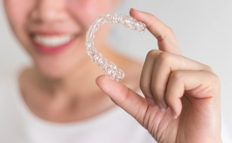 A smiling woman holding an Invisalign aligner in her hand