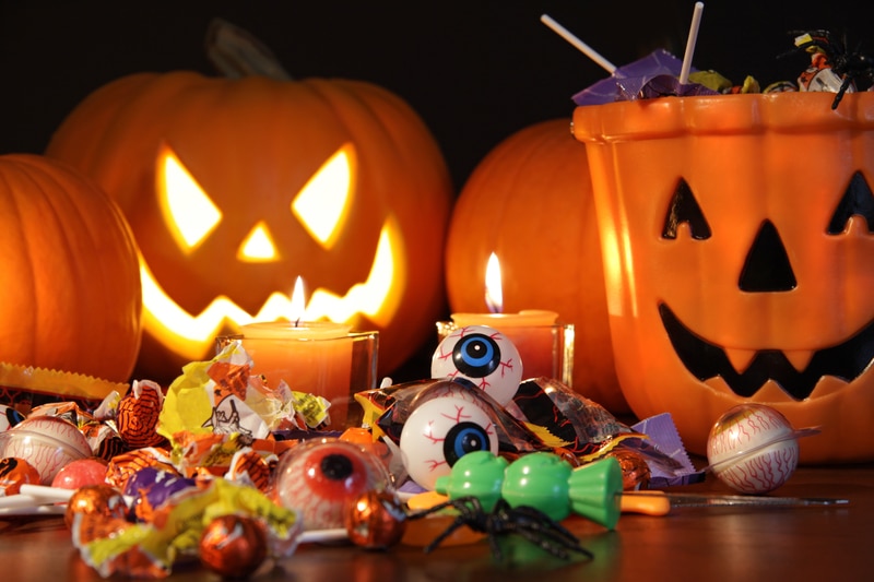 A lit-up jack-o-latern, a candy pumpkin bucket and a bunch of Halloween candy in front of it.