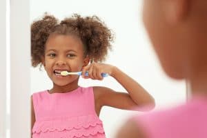 Young African American girl standing in front of a mirror and brushing her teeth.