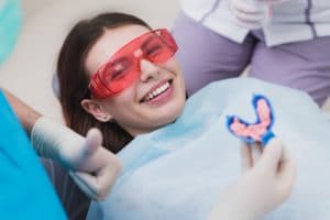 Young woman seated in dental chair about to have fluoride treatment applied to her teeth.