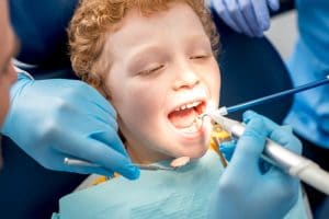 Young boy sitting in dental chair having his teeth cleaned by the dentist.