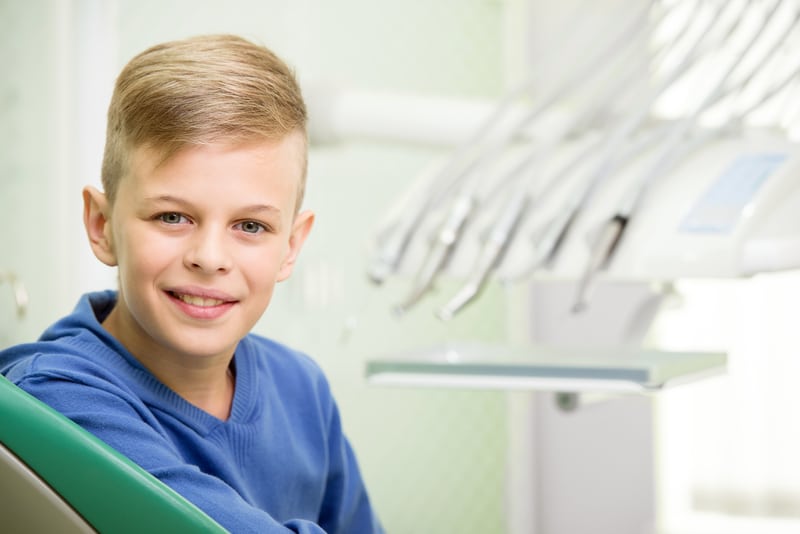 Young boy sitting in dental chair smiling at the camera.