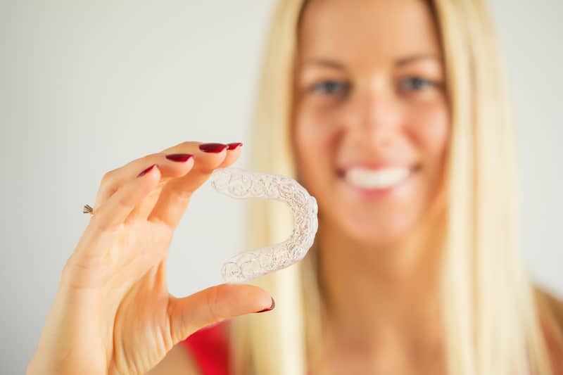 Woman smiling and holding Invisalign aligner