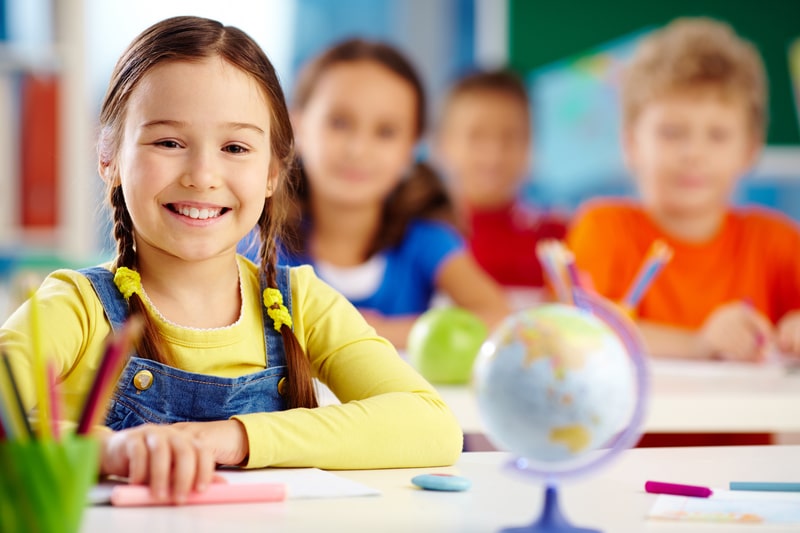 Young girl sitting in school class room with peers all smiling