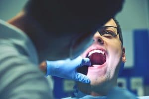 Young man having mouth reviewed by a gloved dentist for signs of oral cancer.