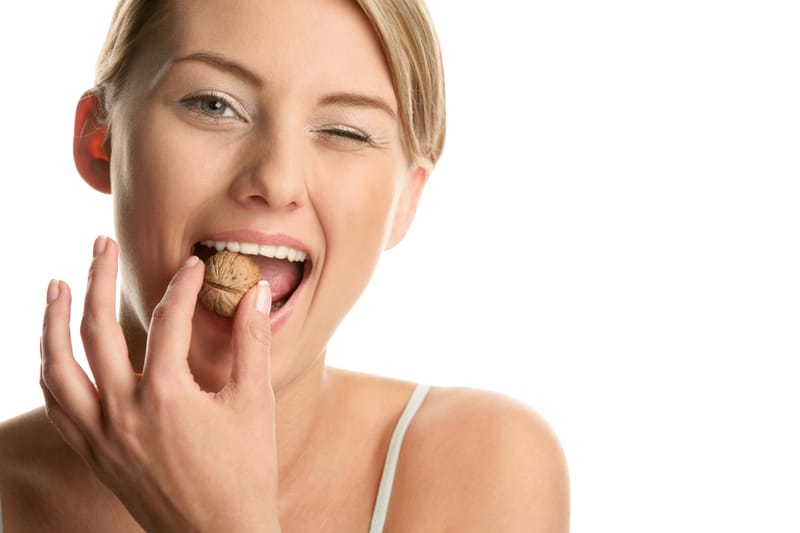 Woman showing how strong her teeth are by biting down on a large walnut shell