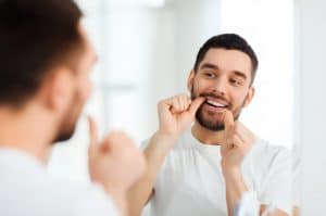 Man flossing teeth in mirror with dental floss.